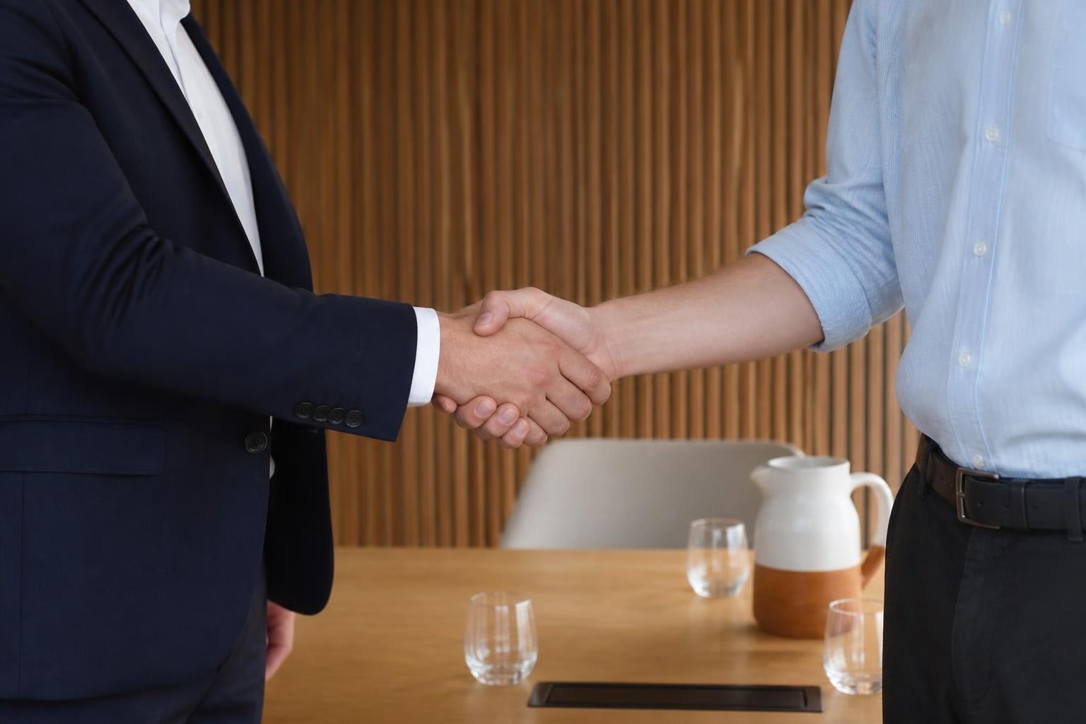 Twee mensen schudden elkaar de hand naast een vergadertafel